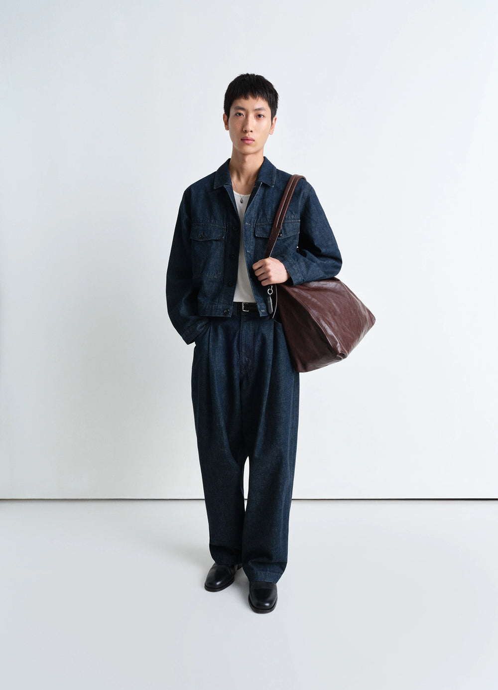 Lemaire Trucker Jacket in Deep Indigo Heavy Denim, model shot, full-body view paired with leather bag