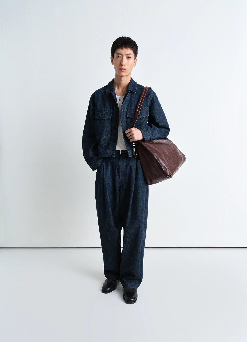 Lemaire Trucker Jacket in Deep Indigo Heavy Denim, model shot, full-body view paired with leather bag