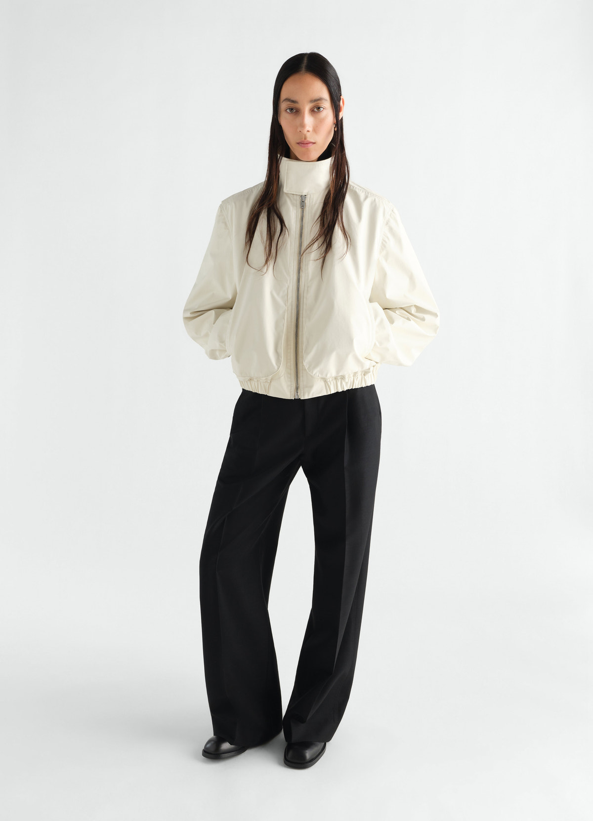 Zipped waterproof cotton blouson in cream by lemaire worn by model with black wide-leg trousers front view