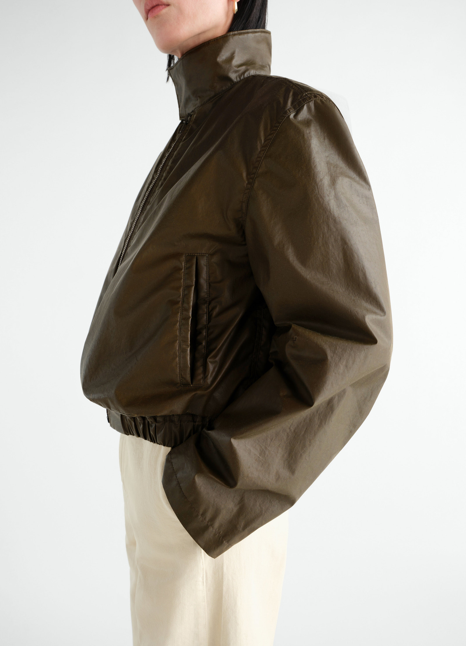 Zipped blouson in dark olive waterproof cotton by lemaire worn by a model side view with high collar and elastic hem