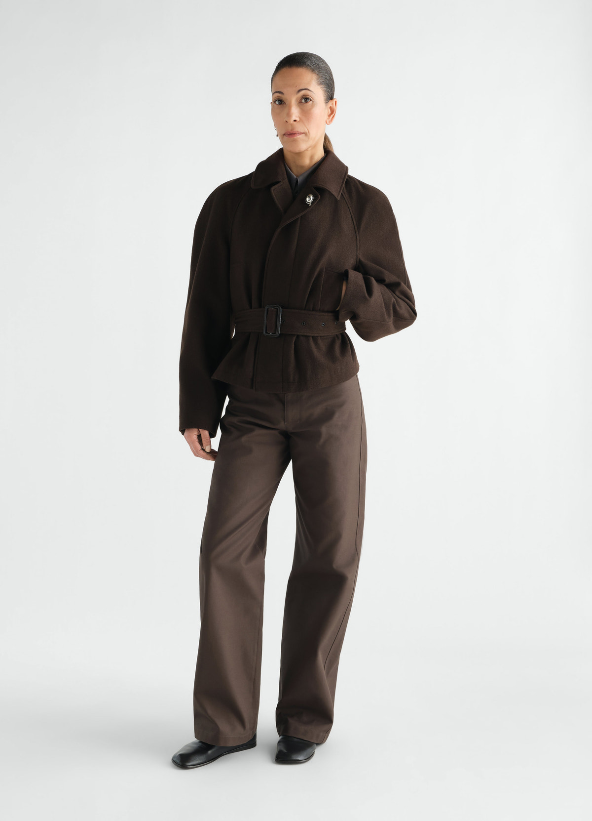 Short brown wool belted coat and cotton twill pants worn by model lemaire front view