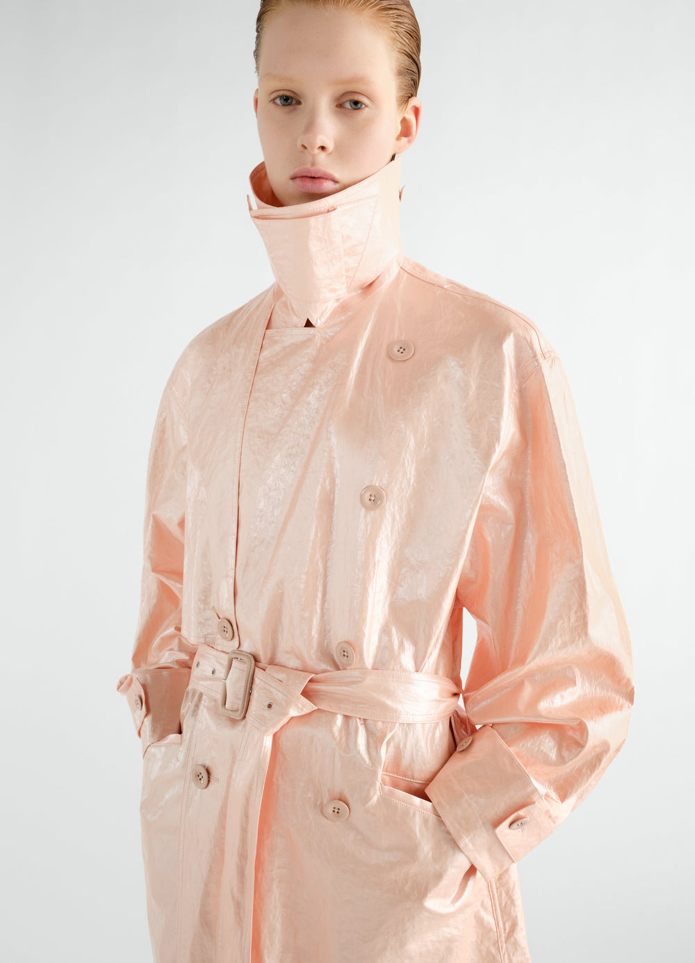Trench coat LEMAIRE peach shiny coated linen with high collar and belt worn by a model front view
