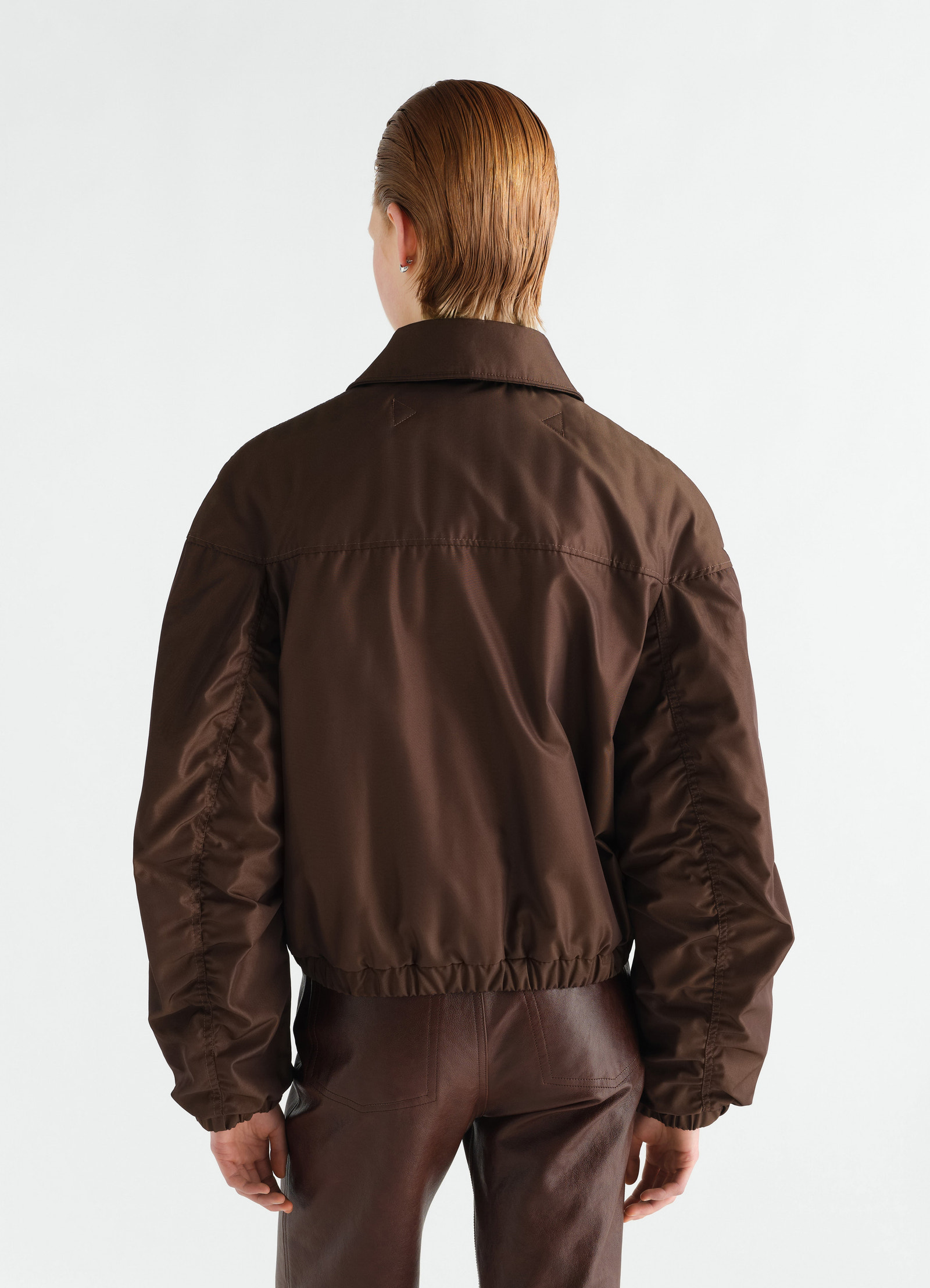 Quilted blouson in brown water-repellent canvas lemaire, back view worn by a model with matching brown leather pants