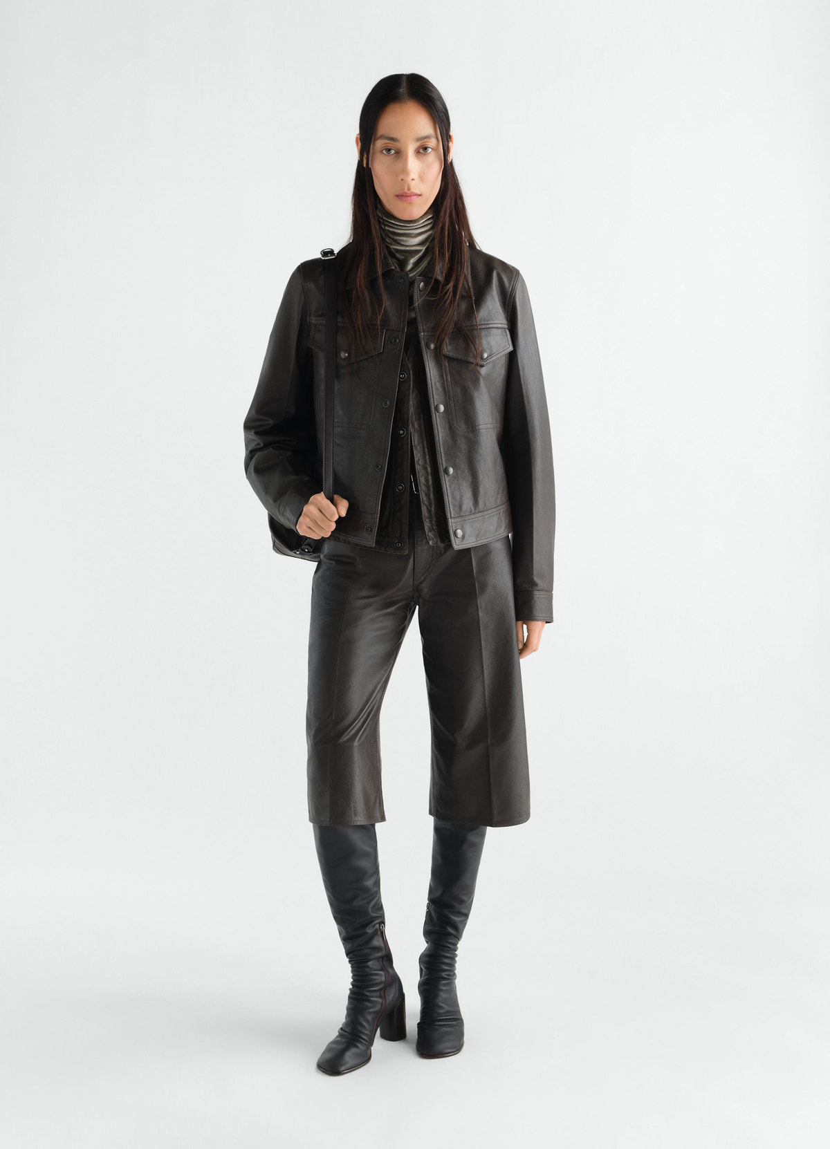 Trucker jacket in glossy black leather by lemaire worn by model with matching leather shorts and boots