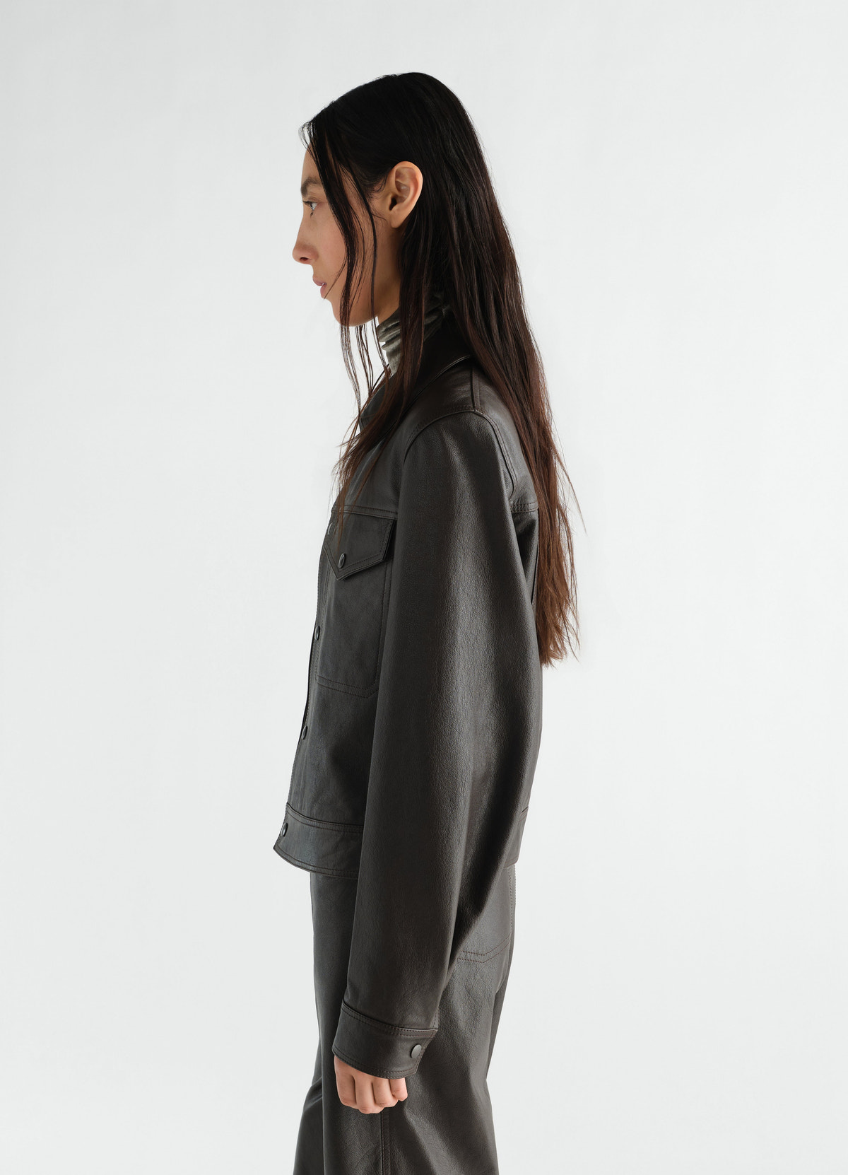Trucker jacket in glossy black leather by lemaire worn by model side view on white background
