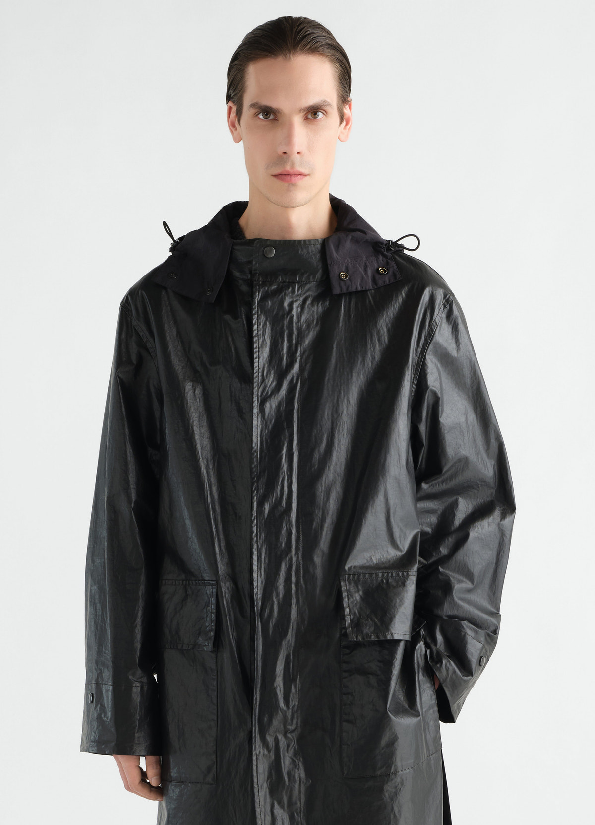 Long black coated linen cotton blend raincoat by lemaire worn by model front view with hood and pockets