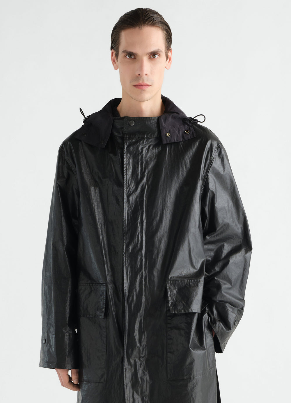 Long black coated linen cotton blend raincoat by LEMAIRE worn by model front view with hood and pockets