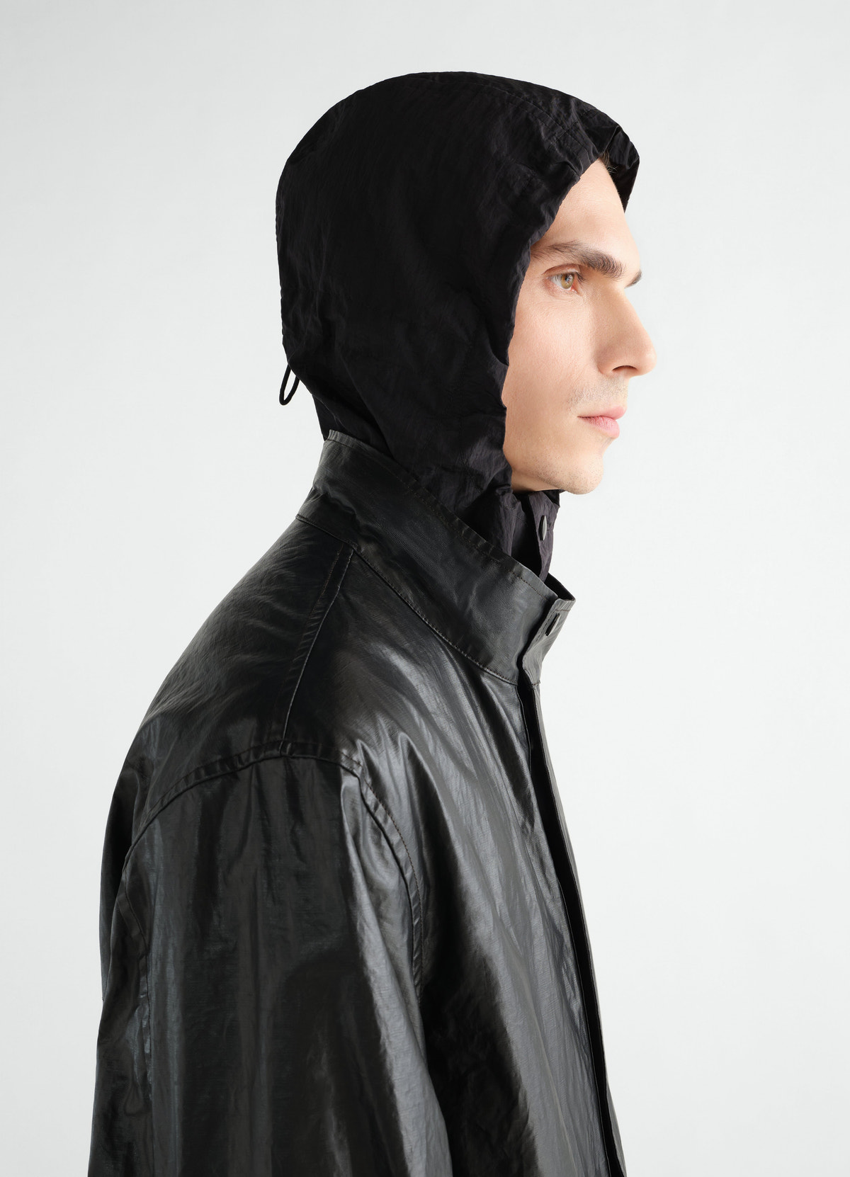 Long black coated linen cotton blend raincoat by lemaire worn by model side view with hood up