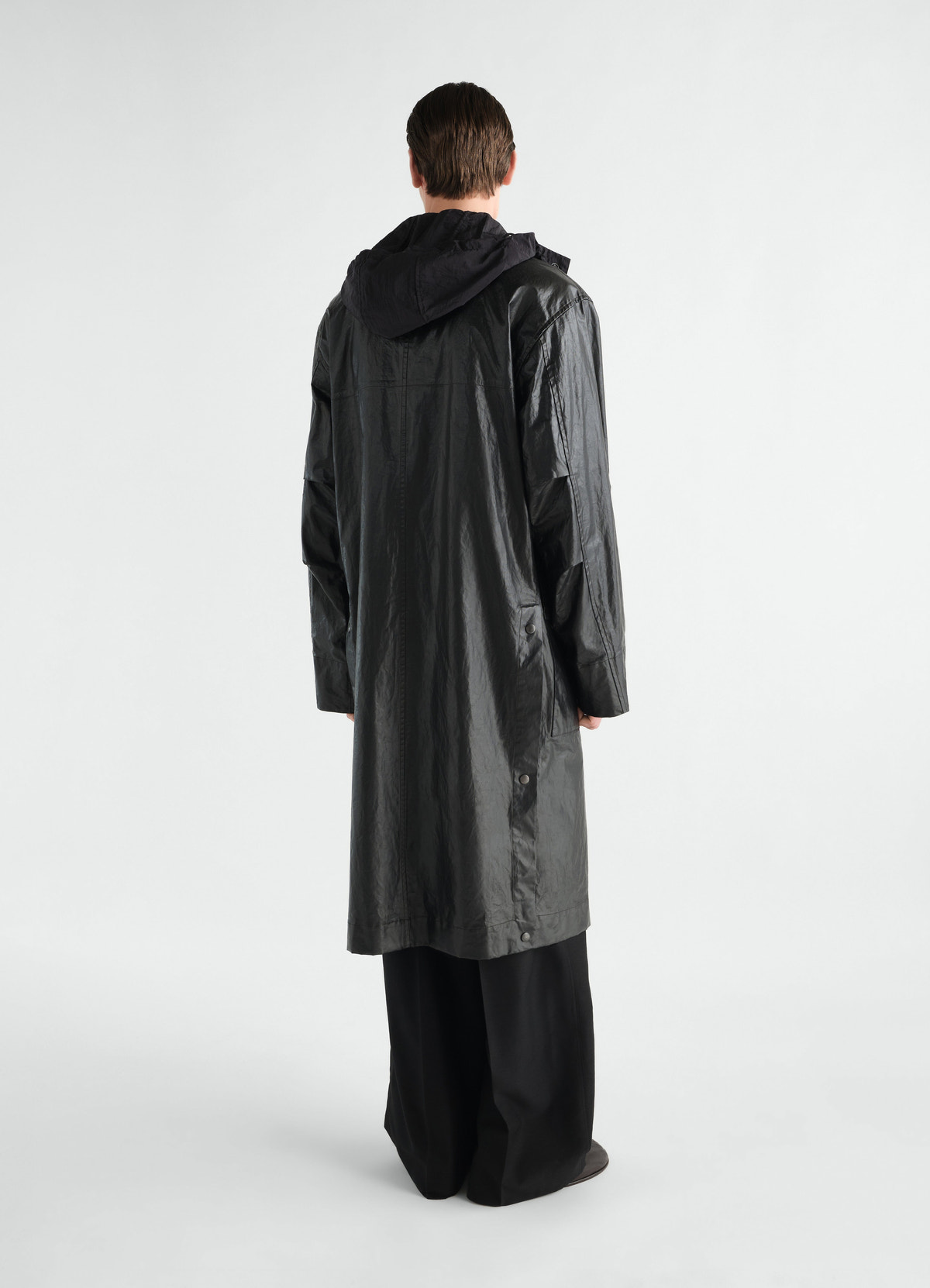 Long black coated linen and cotton blend raincoat by lemaire worn by model back view with hood