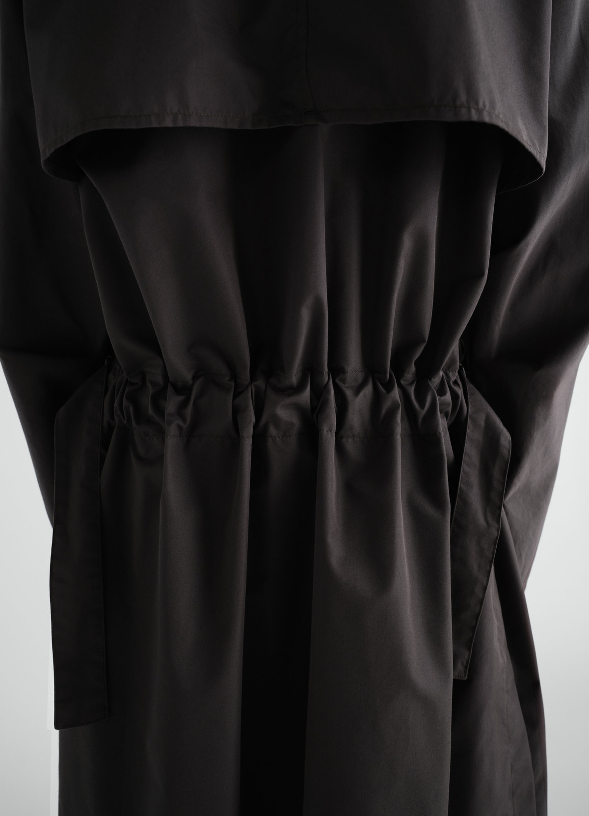 Light black cotton gabardine trench coat by lemaire with gathered back detail worn by a model, close-up back view