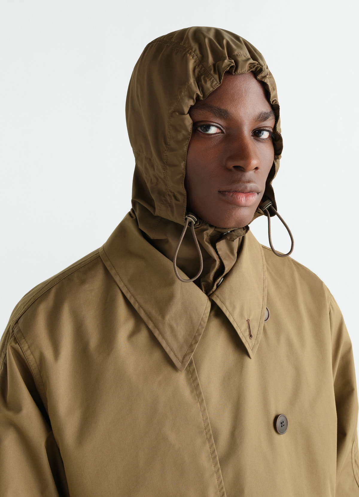 Light brown water-repellent cotton gabardine trench coat with hood worn by a model lemaire front close-up
