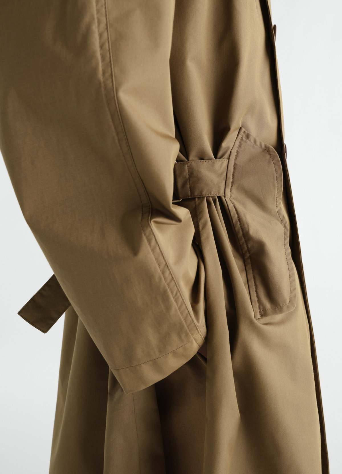 Light brown water-repellent cotton gabardine trench coat by lemaire, close-up side pocket and sleeve detail worn by model