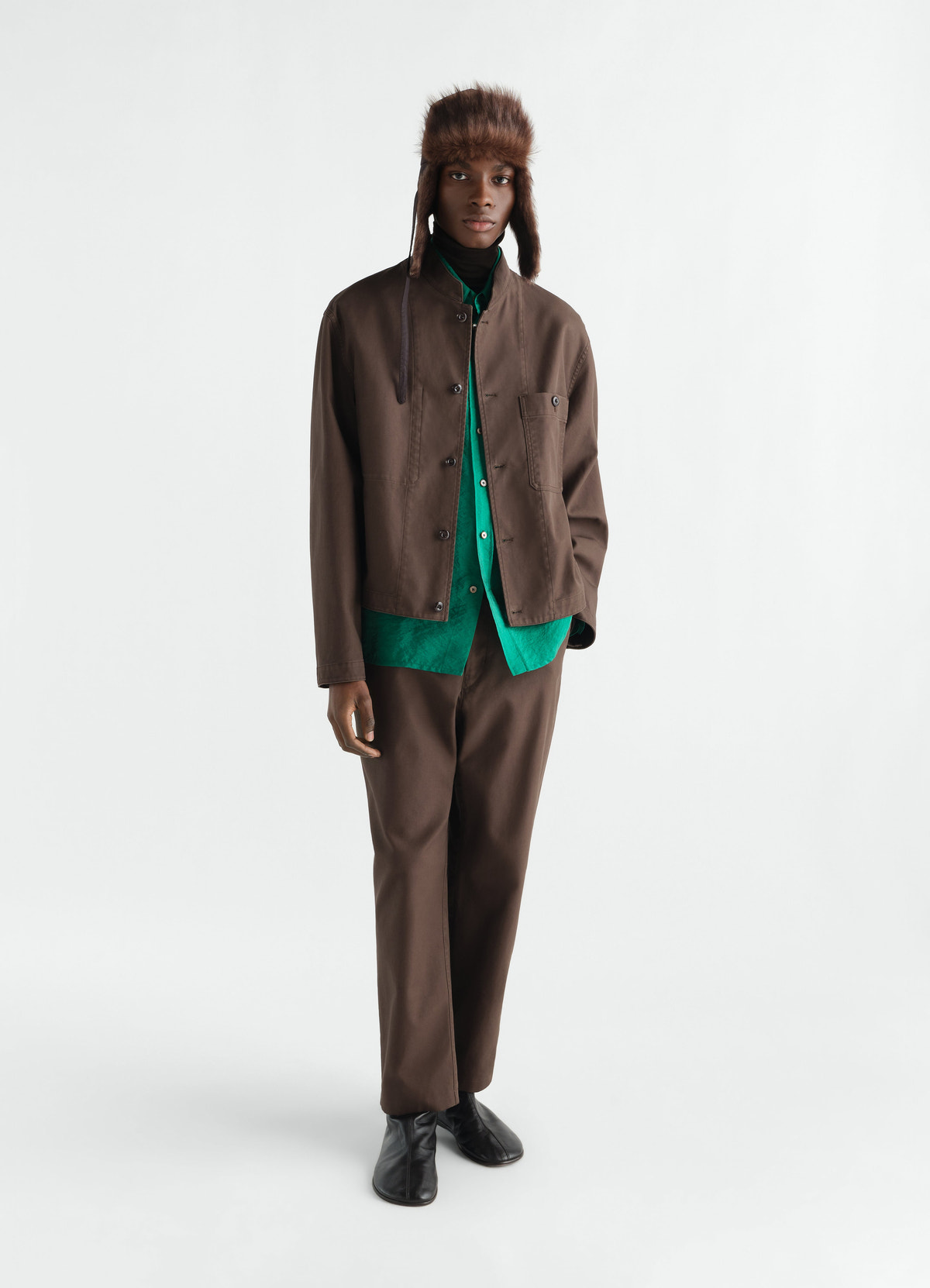 Stand-collar brown cotton twill jacket by lemaire worn by model with green shirt and hat in styled look
