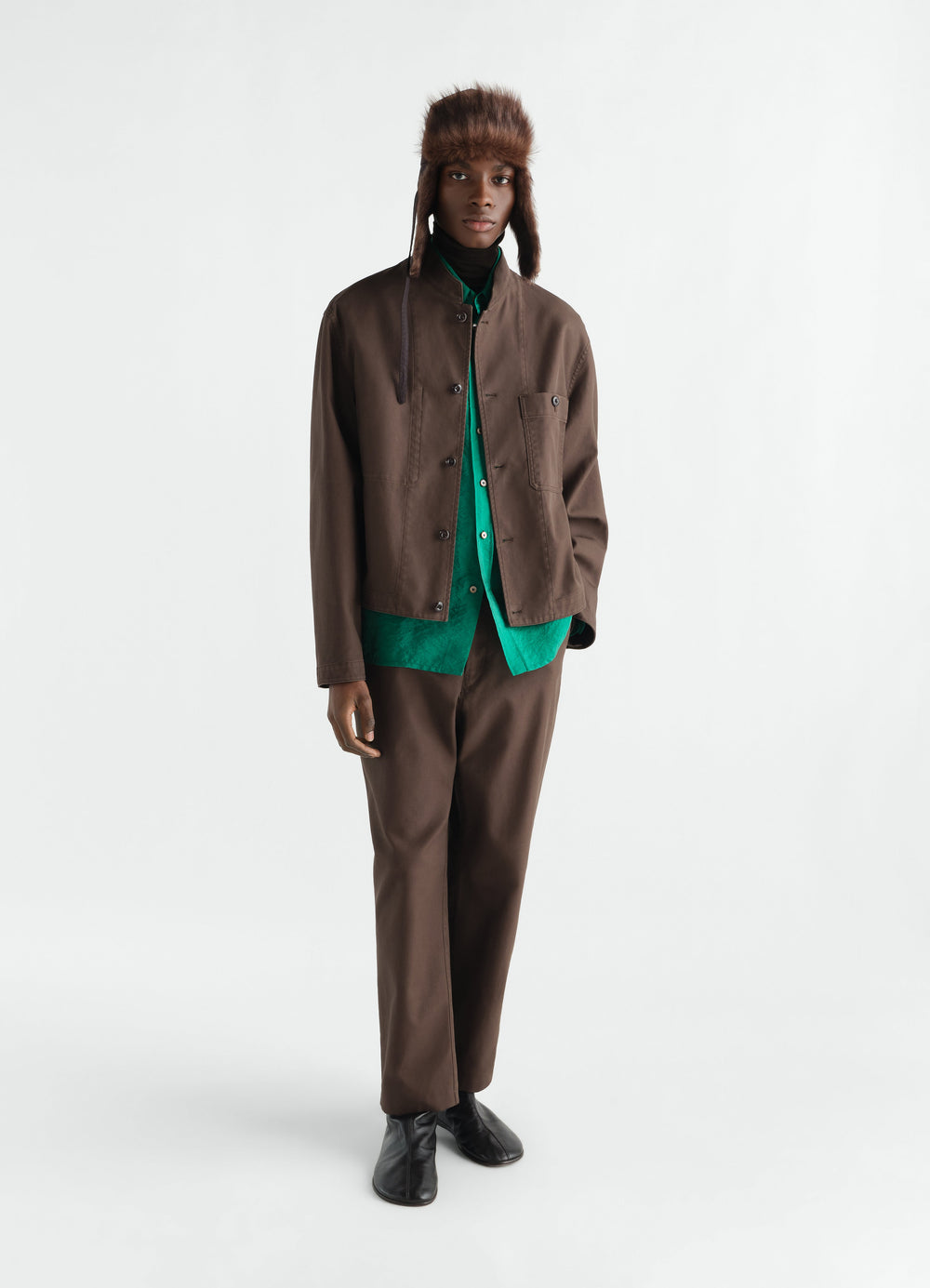 Stand-collar brown cotton twill jacket by LEMAIRE worn by model with green shirt and hat in styled look