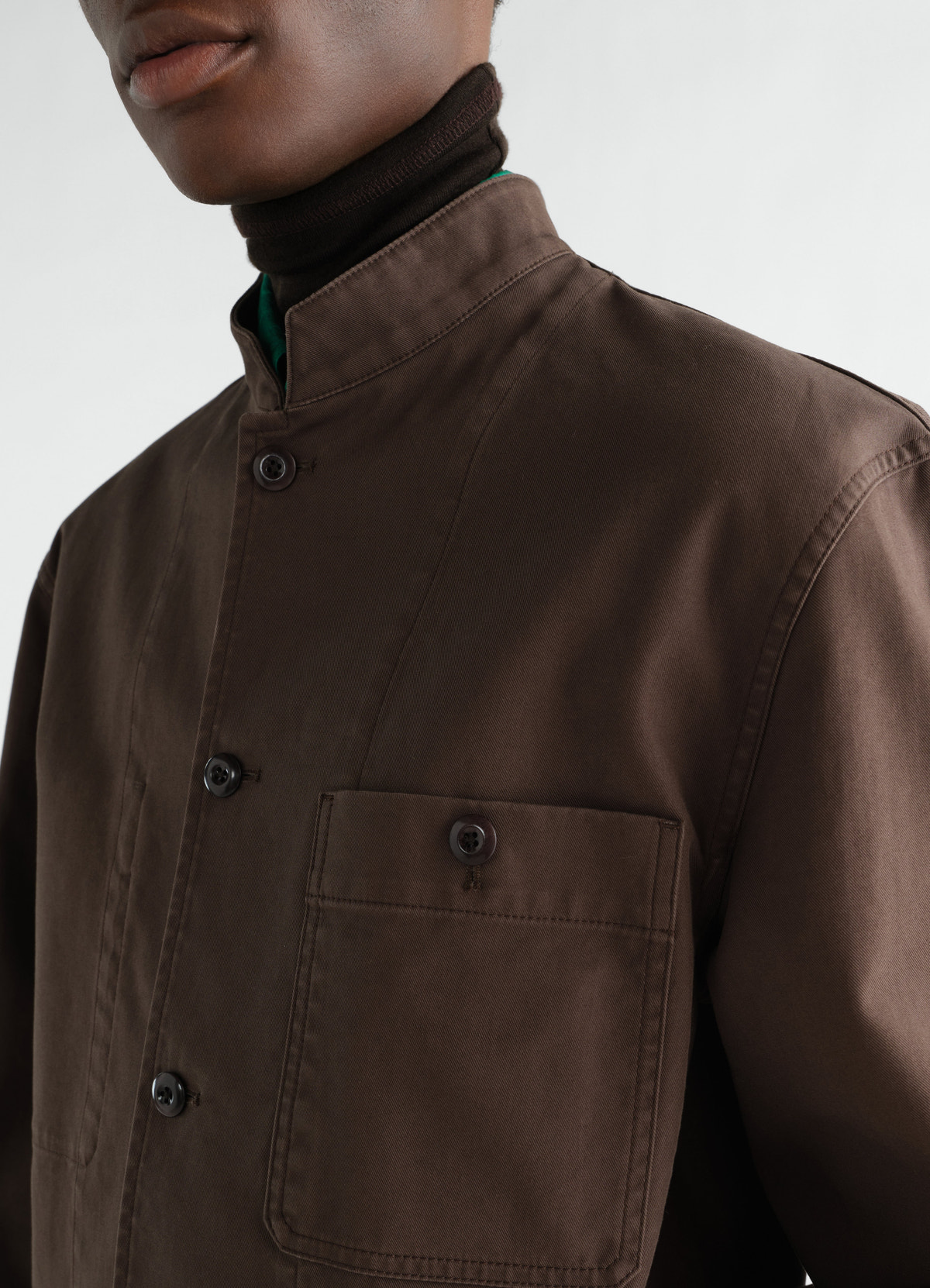 Stand-collar heavy cotton twill jacket in dark brown by lemaire worn by a model close-up front detail
