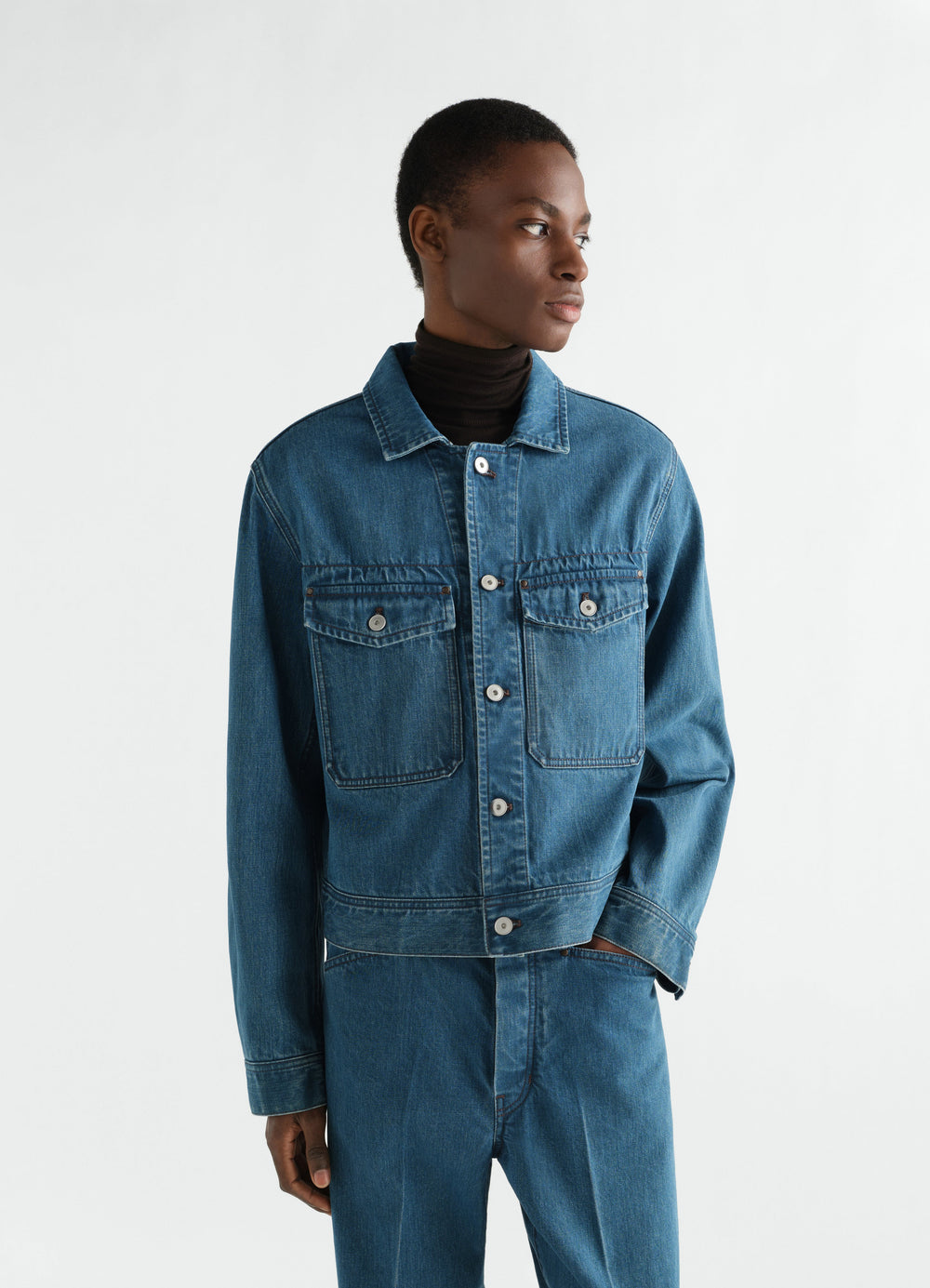 Trucker jacket in indigo selvedge denim by LEMAIRE worn by model front view with button closure and flap pockets