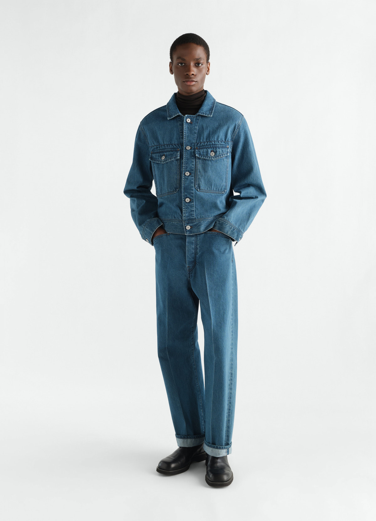 Trucker jacket in indigo selvedge denim by lemaire worn by model with matching jeans on white background