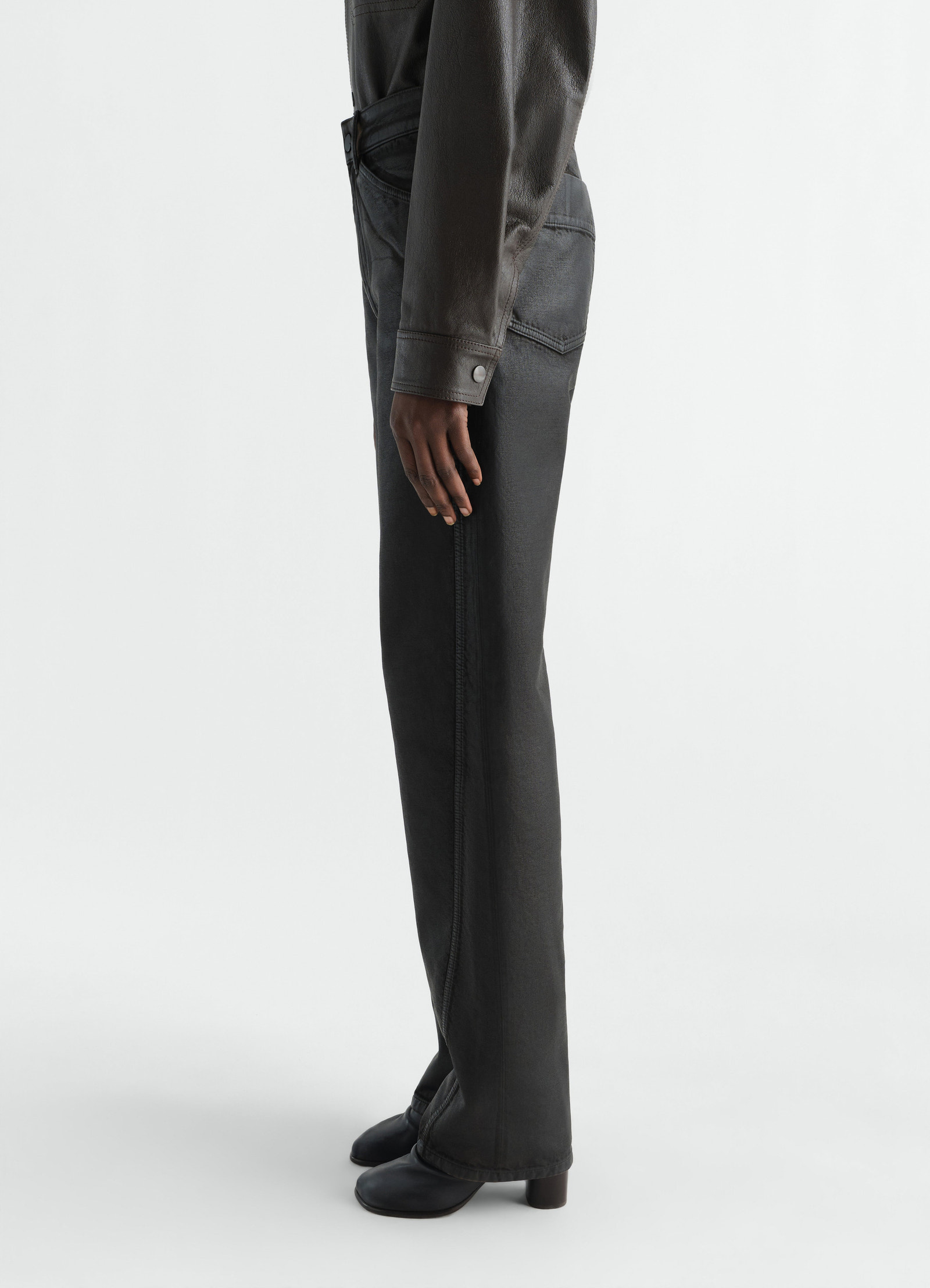 Twisted five-pocket black coated denim pants lemaire worn by model side view with black boots