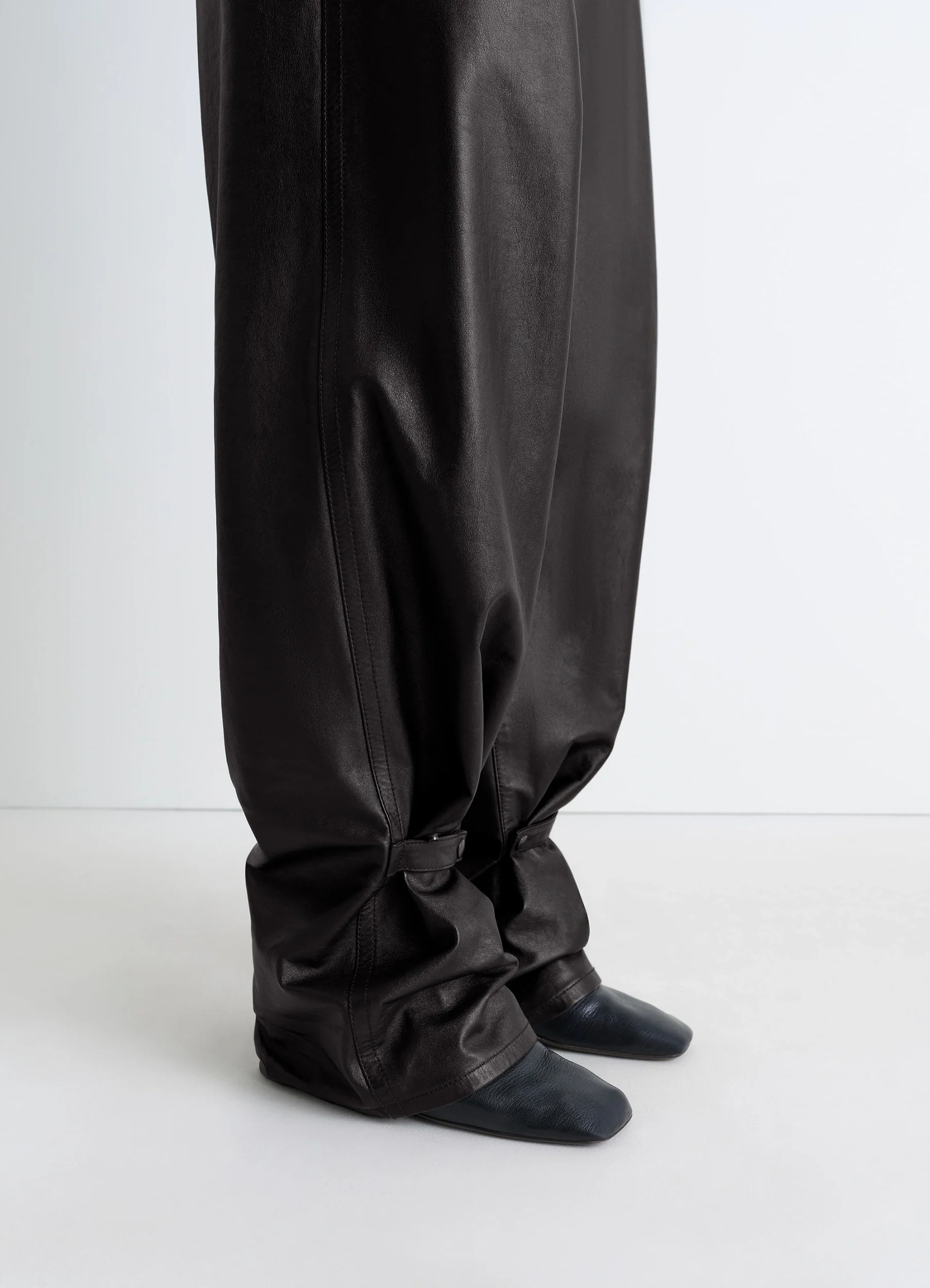 Lemaire soft leather pants in cow leather with natural shine, model shot, detail shot of lower legs slouchy fit with strap