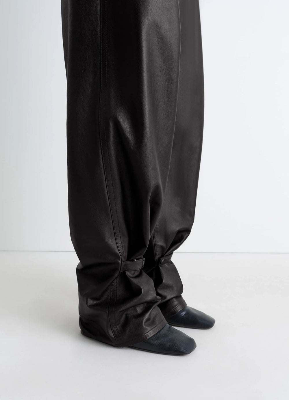 Lemaire Soft Leather Pants in Cow leather with natural shine, model shot, detail shot of lower legs slouchy fit with strap