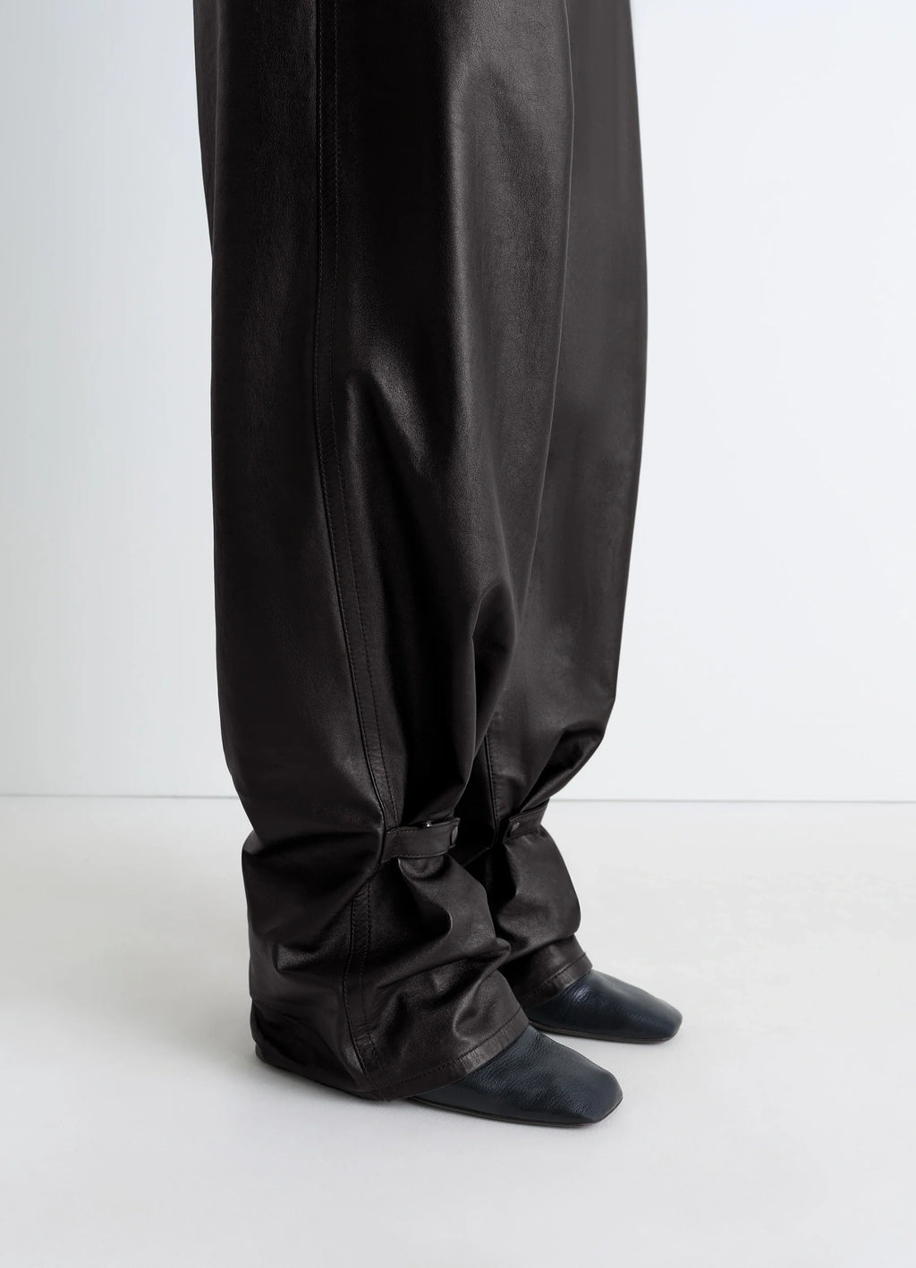 Lemaire Soft Leather Pants in Cow leather with natural shine, model shot, detail shot of lower legs slouchy fit with strap