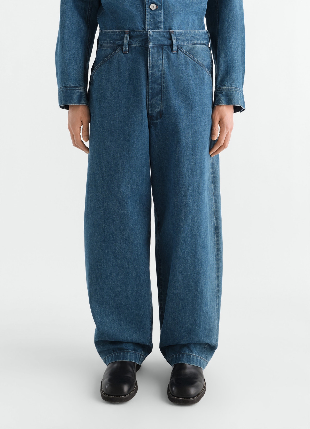 Oversized indigo selvedge denim pants lemaire front worn by model with black shoes and denim shirt
