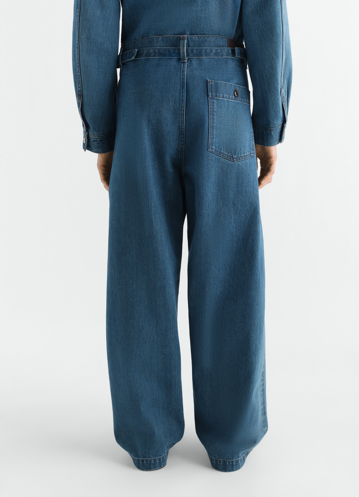 Oversized indigo selvedge denim pants with back pocket and belt, worn by model lemaire back view