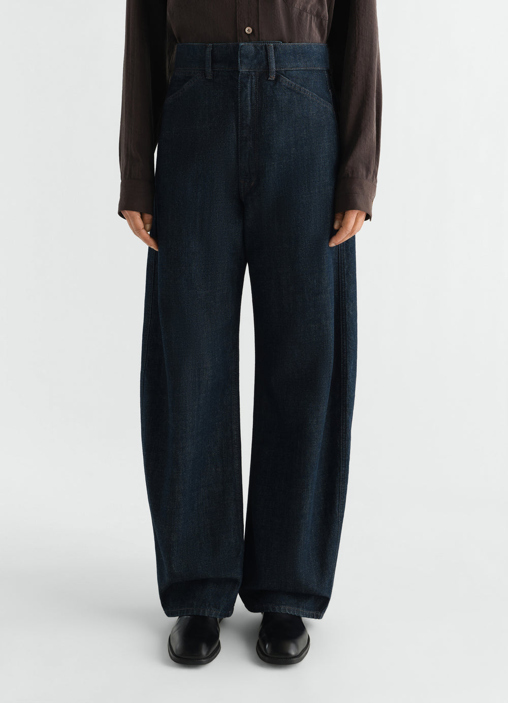 High waisted dark blue denim curved pants by LEMAIRE worn by a model front view with black shoes