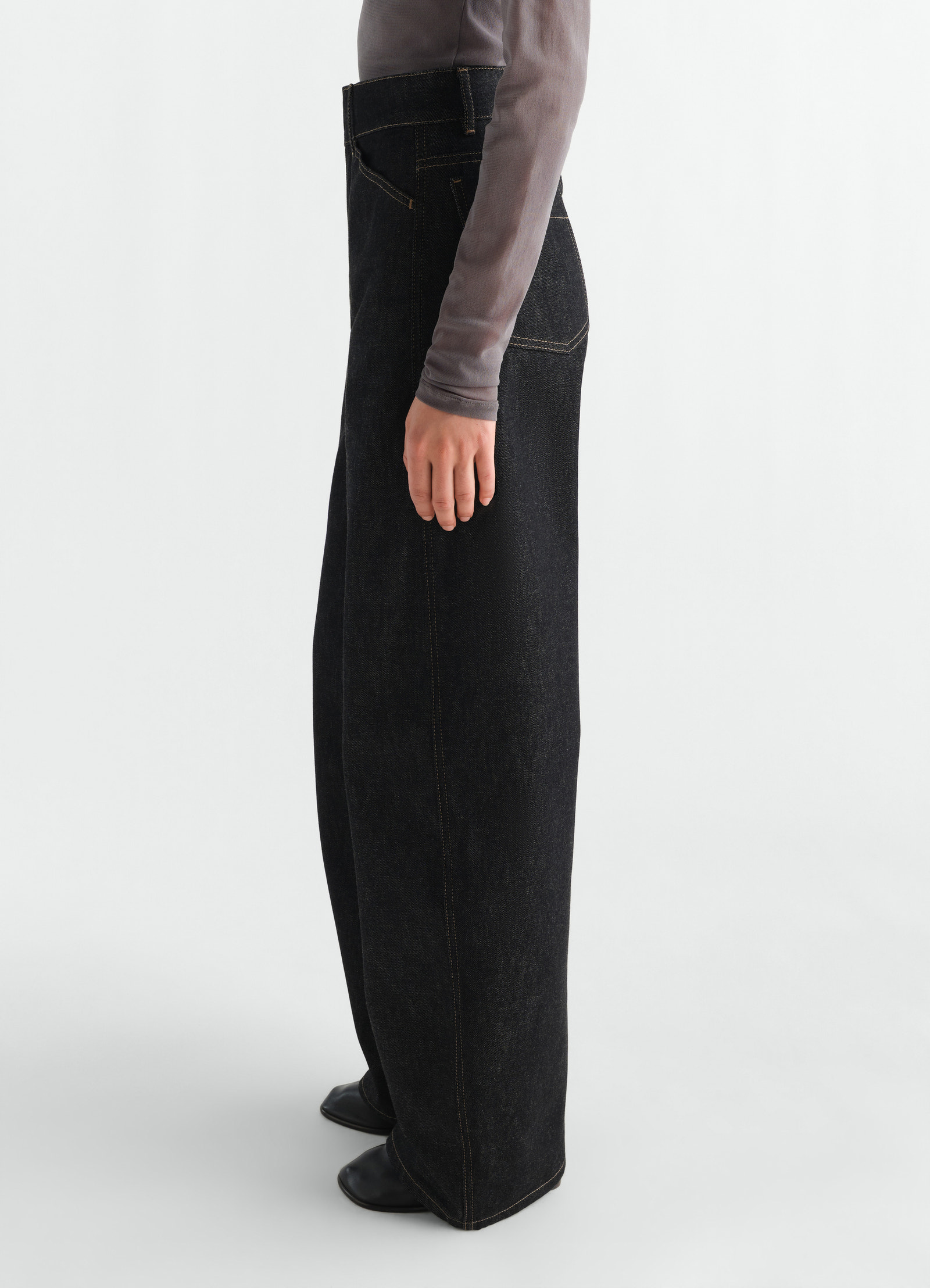 High waisted black denim curved pants with contrast stitching by lemaire worn by a model side view