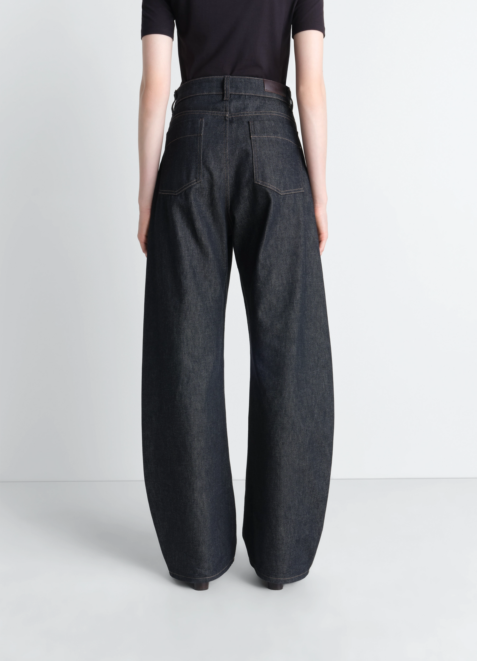 Lemaire high waisted curved pants in slate denim, model shot, angled back view curved hemline, rear pocket detail