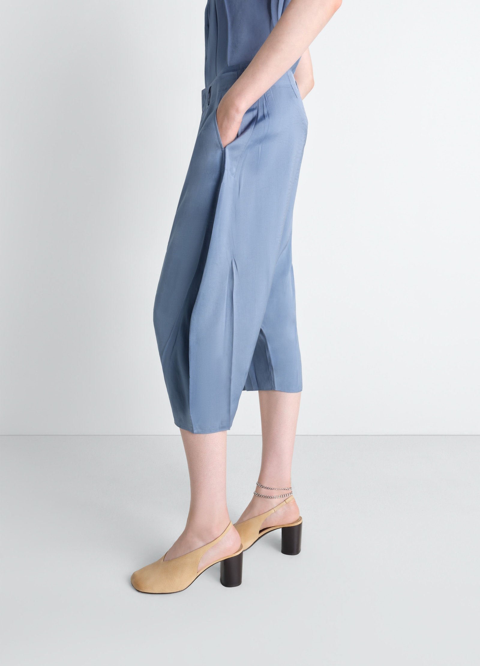 Creased dropped crotch bermudas in poly viscose twill, model shot, three-quarter view flowing hem, cropped length