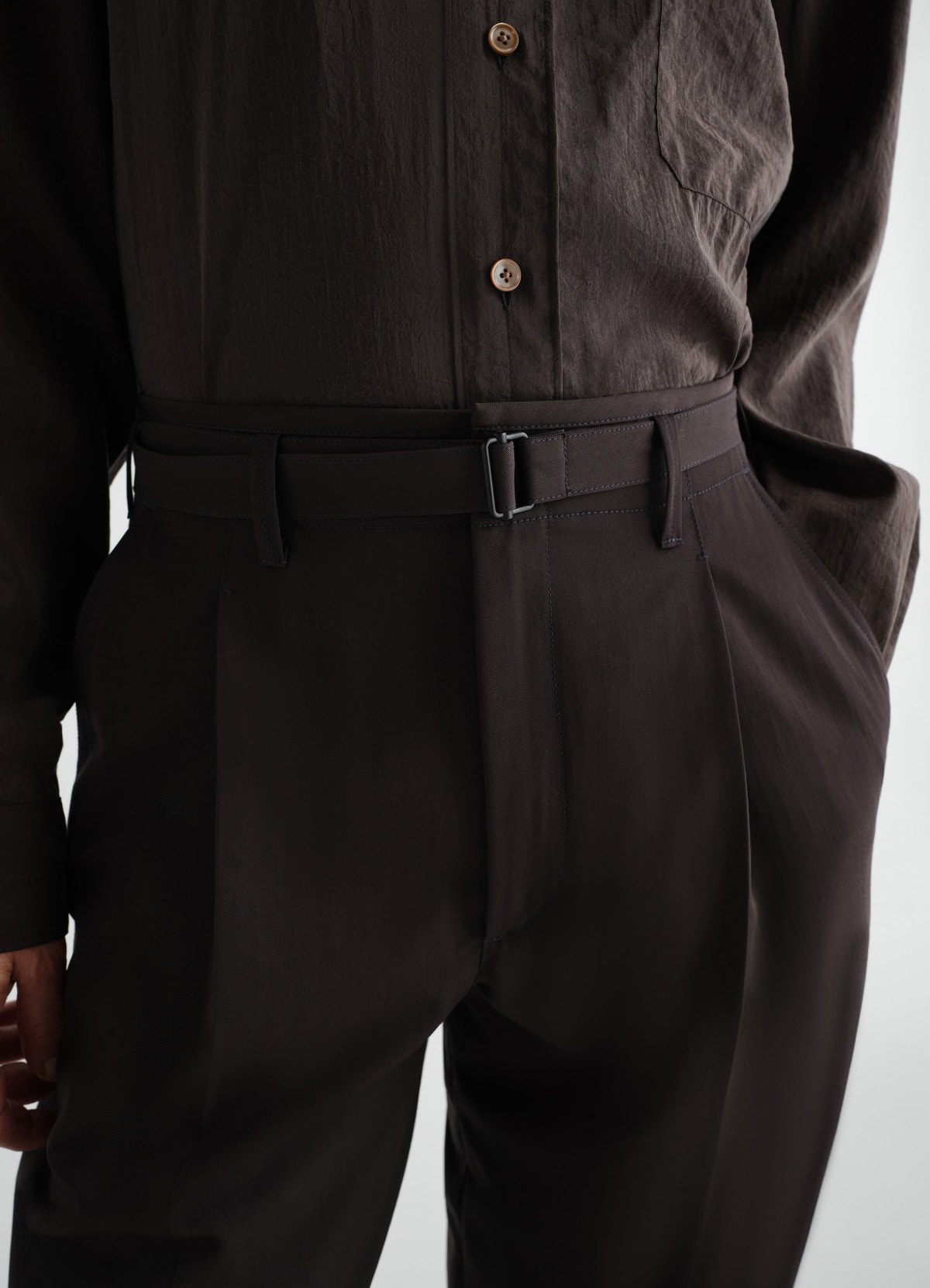 Wide pleated dark brown wool gabardine pants with belt, worn by model, front close-up detail lemaire