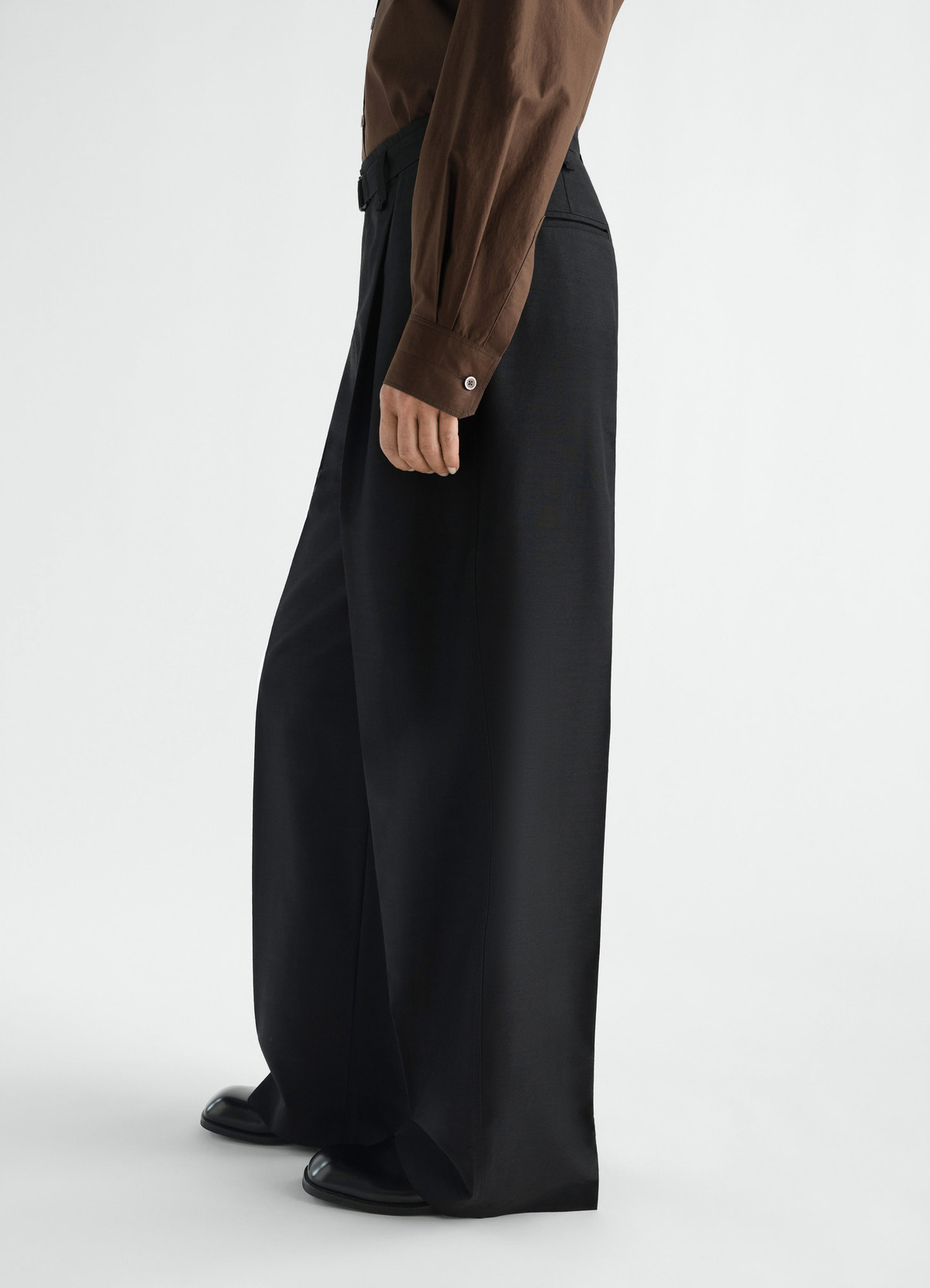 Wide black wool mohair cloth pants lemaire worn by model side view with pleated front and belt detail