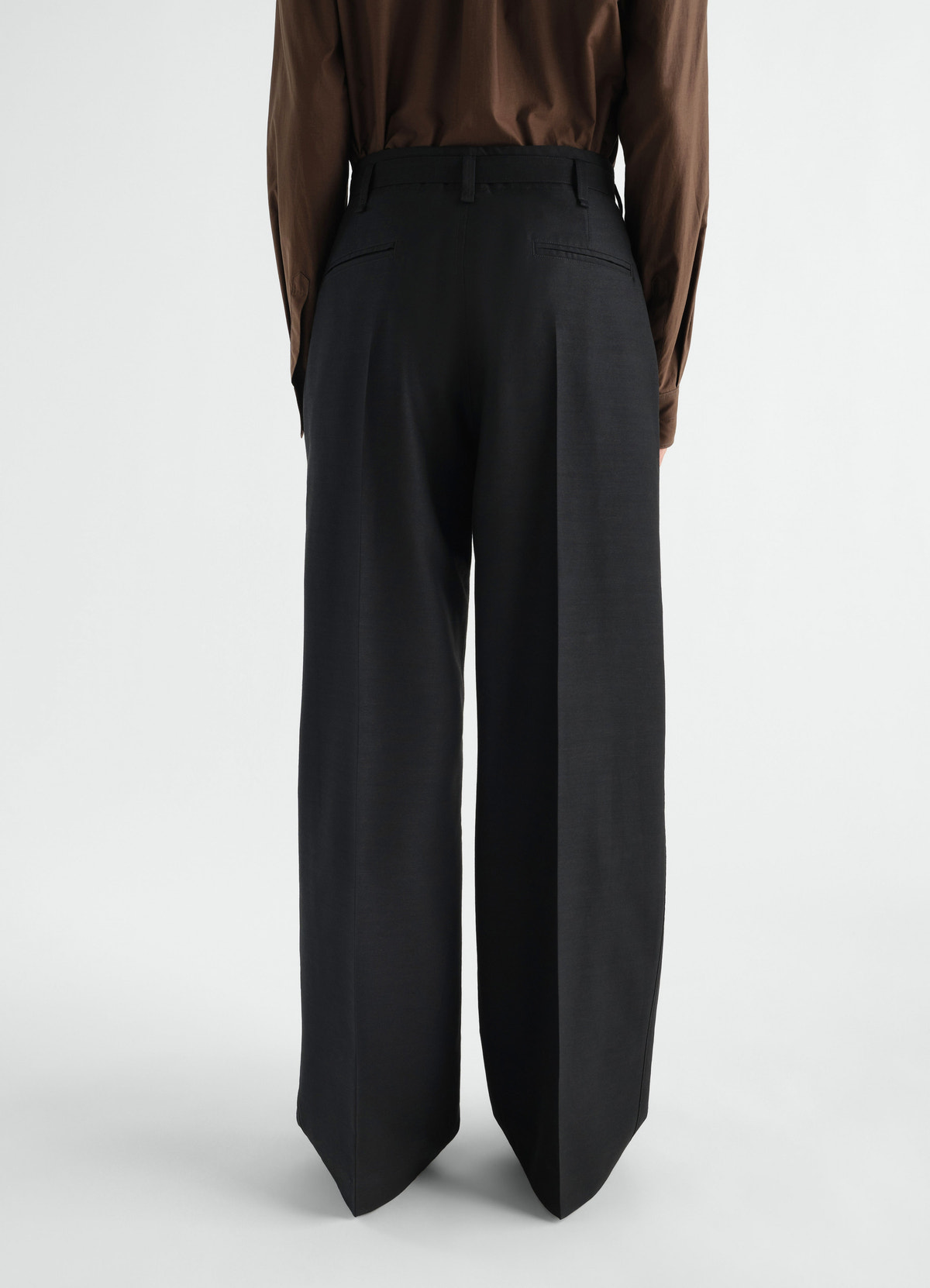 Wide black wool mohair pants with pleats lemaire worn by model back view on white background