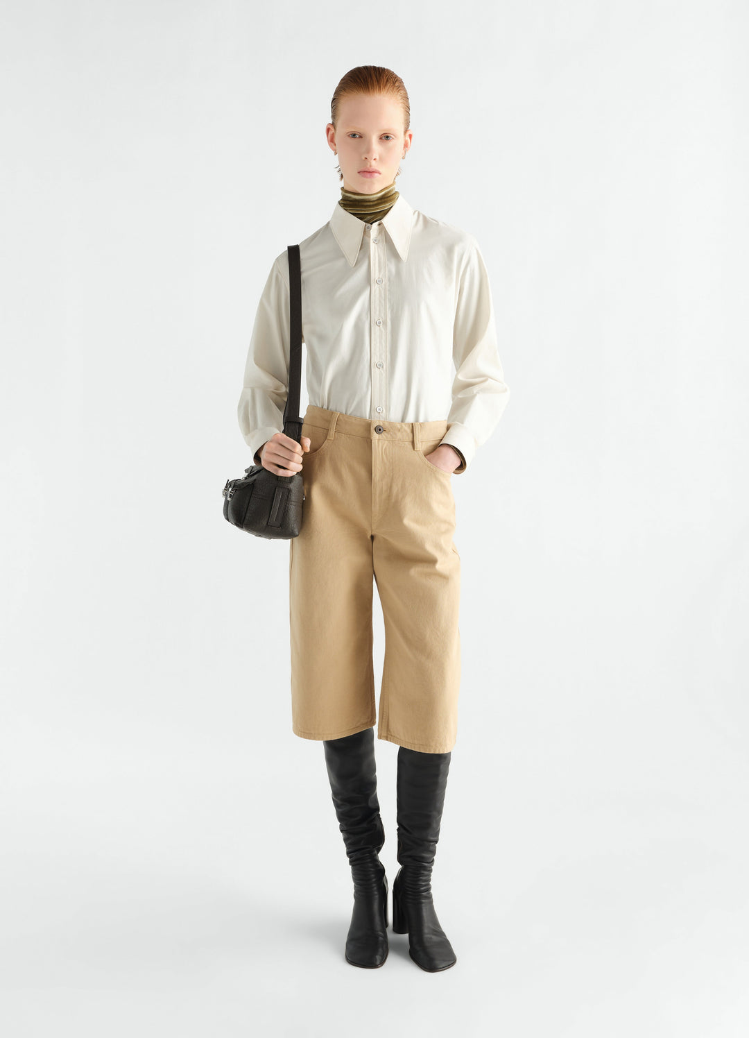 Five-pocket beige cotton Bermuda shorts by LEMAIRE worn by model front view with black boots and bag