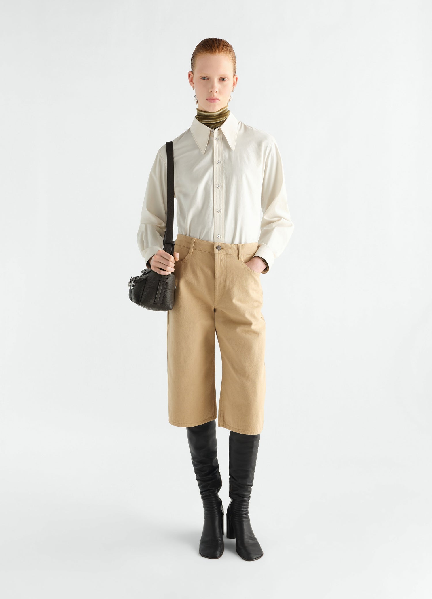 Five-pocket beige cotton Bermuda shorts by LEMAIRE worn by model front view with black boots and bag