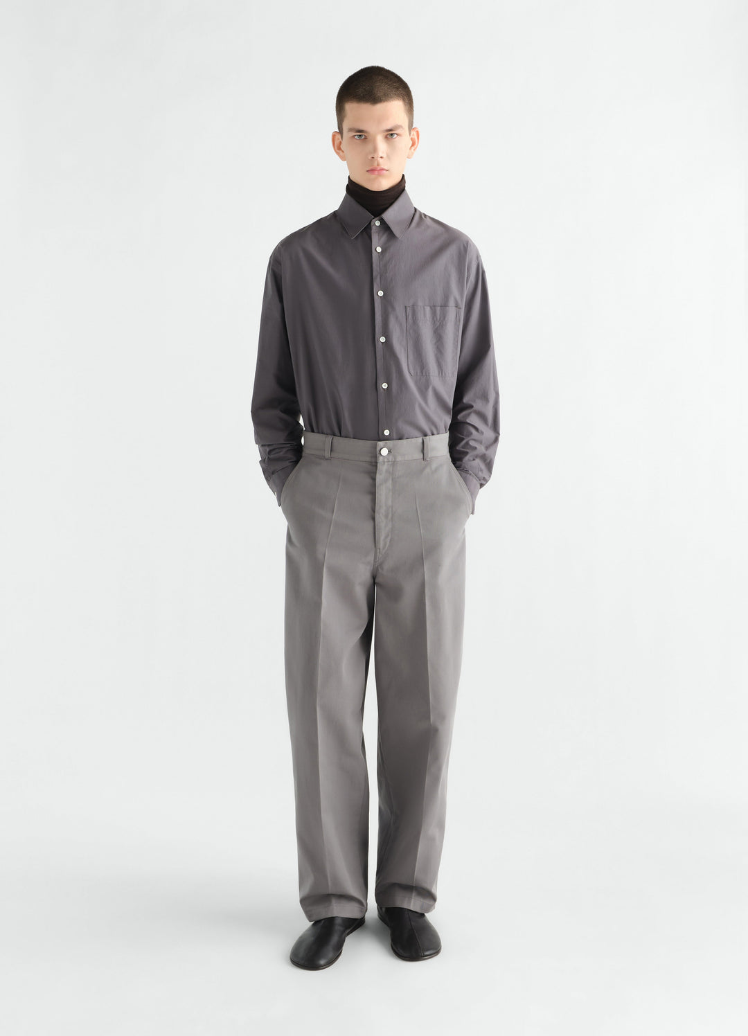 Barrel pants in grey polycotton twill by LEMAIRE worn by model front view with black shoes and tucked shirt