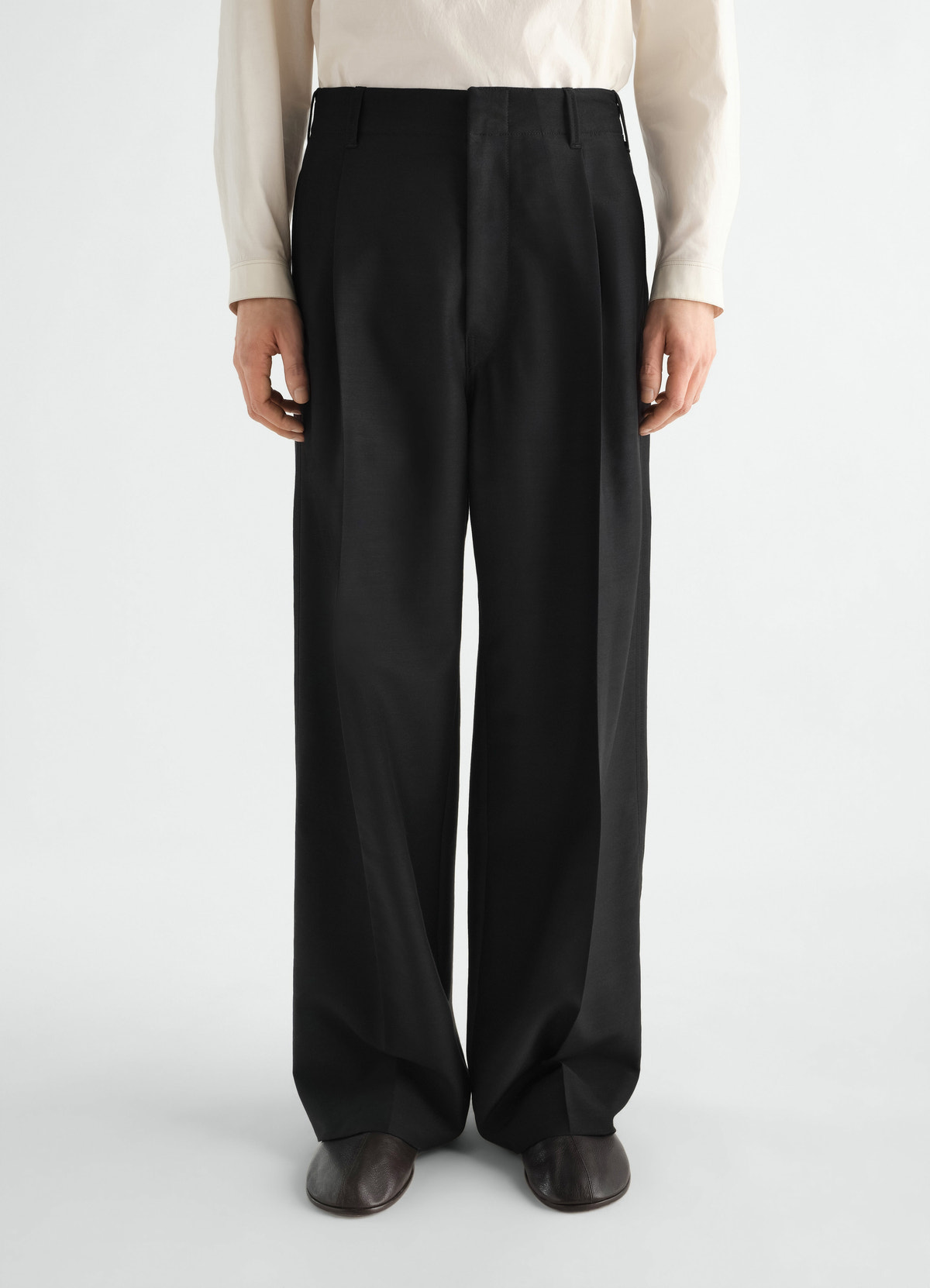 Single-pleat black wool and mohair lemaire tailored pants worn by model front view with off-white shirt