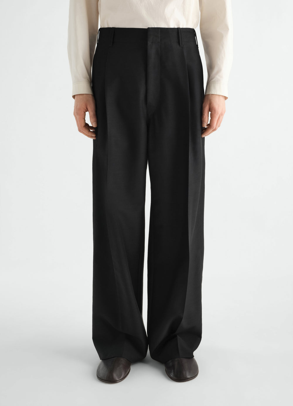 Single-pleat black wool and mohair LEMAIRE tailored pants worn by model front view with off-white shirt