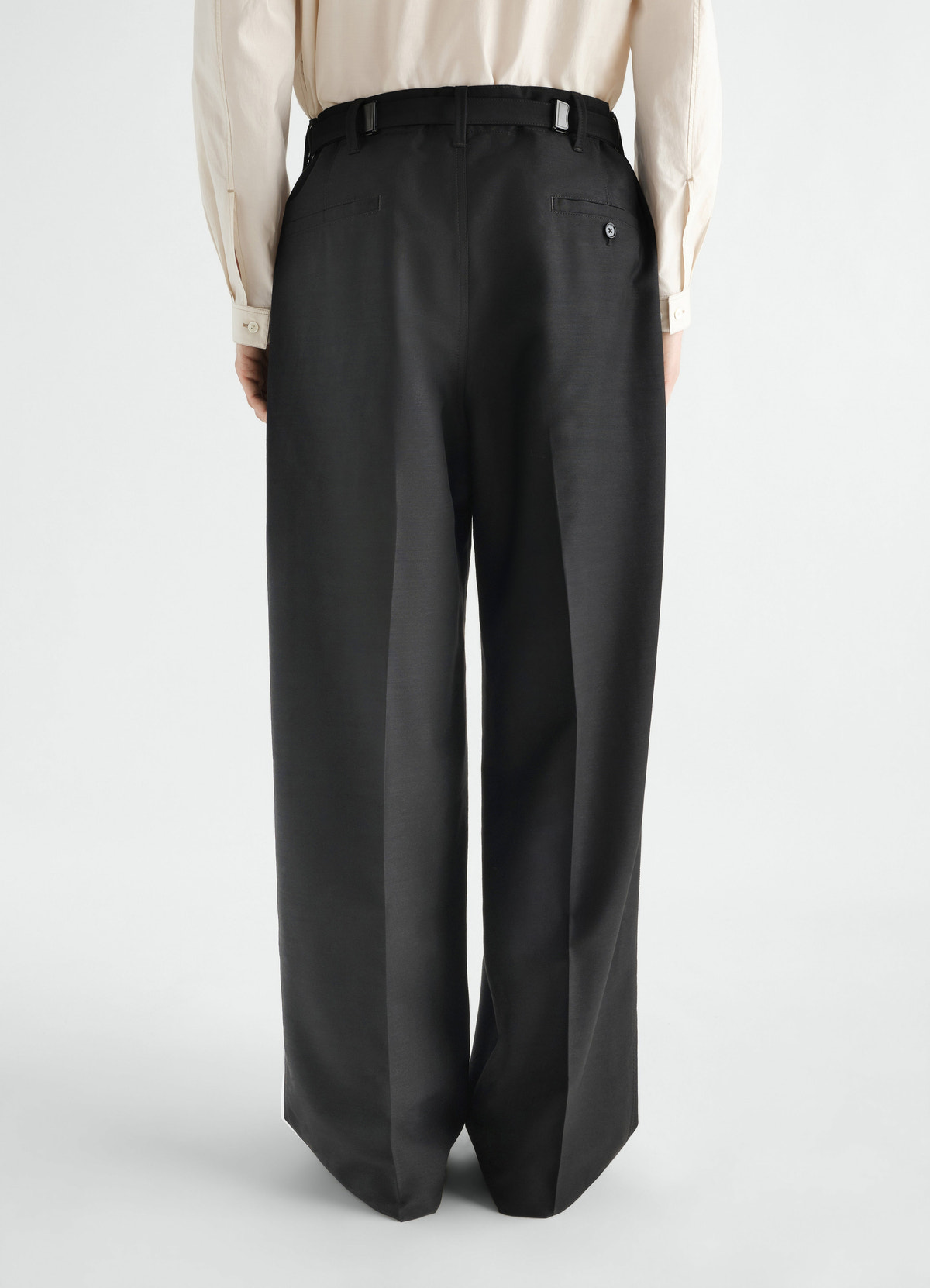 Single-pleat black wool mohair pants by lemaire worn by model back view with button back pockets and belt loops