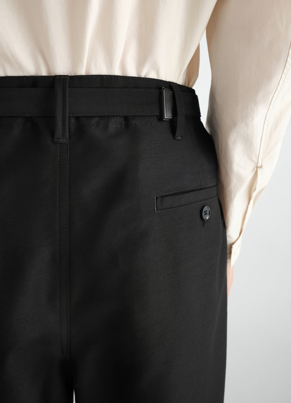 Single-pleat black wool and mohair pants with buttoned back pocket by lemaire worn by model side detail