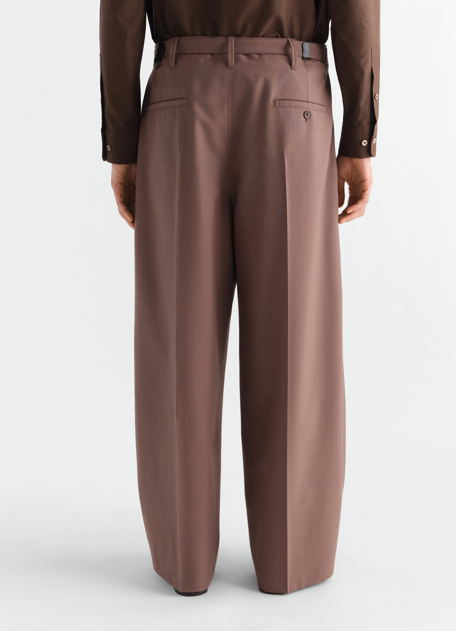 Single-pleat tailored brown wool blend pants by lemaire worn by model back view with buttoned pockets and belt loops