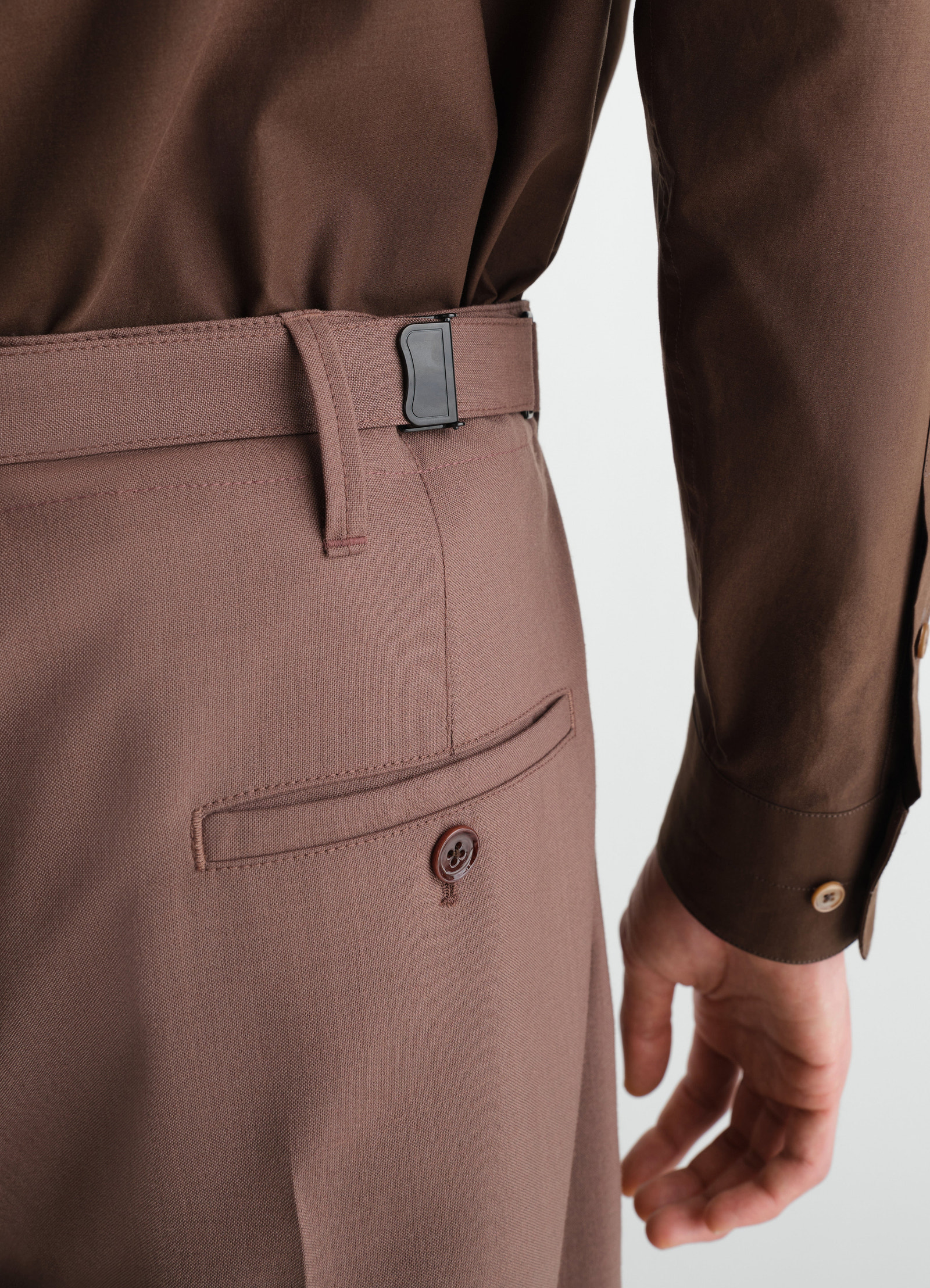 Single-pleat tailored tropical wool blend pants in mauve brown worn by model showing side buckle and back pocket by lemaire