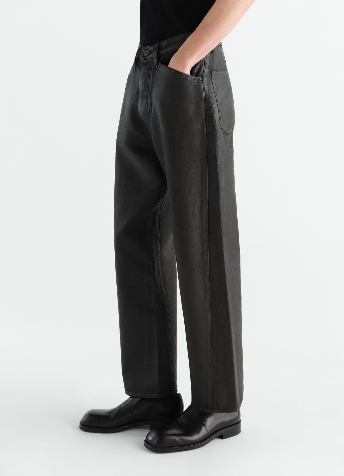 Gerade hose mit fünf taschen aus beschichtetem denim, in schwarz, von einem model getragen, seitenansicht, taschen sichtbar