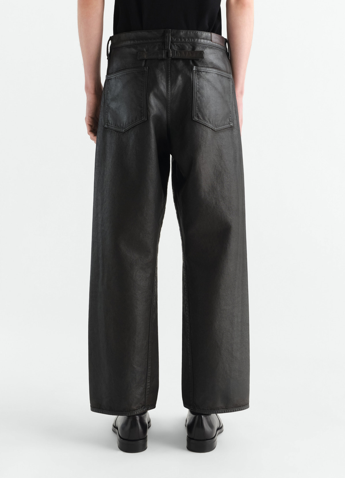 Gerade hose mit fünf taschen aus beschichtetem denim, in schwarz, von einem model getragen, rückansicht, taschen sichtbar