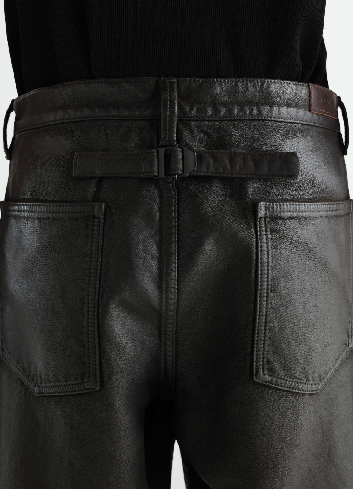 Gerade hose mit fünf taschen aus beschichtetem denim, in schwarz, von einem model getragen, taschen sichtbar, schnalle sichtbar