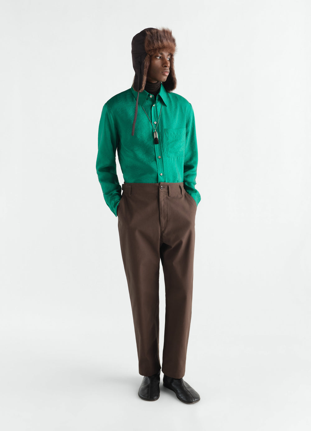 Tapered brown heavy cotton twill pants LEMAIRE worn by model with green shirt and fur hat front view