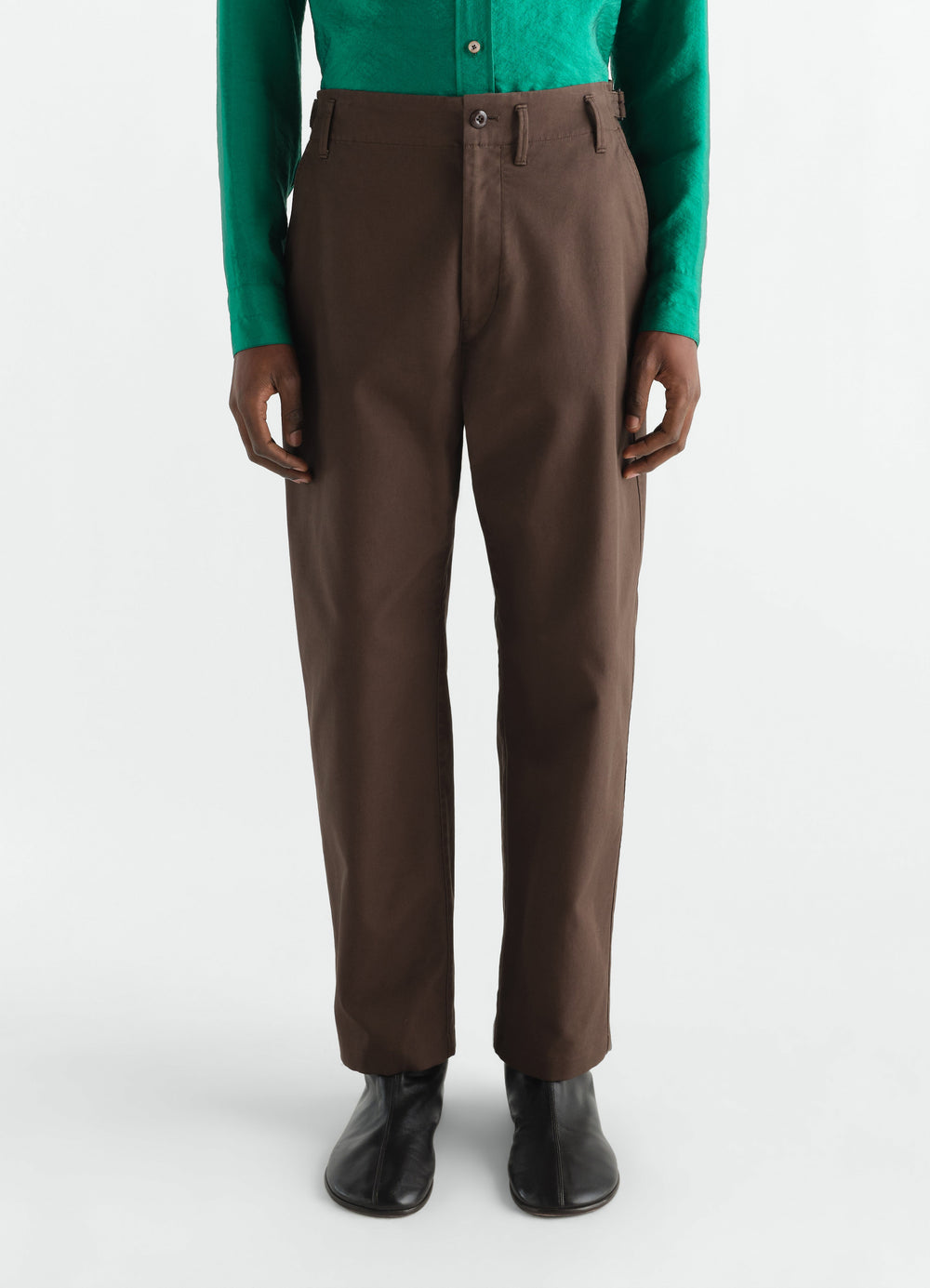 Tapered brown heavy cotton twill pants by LEMAIRE worn by model front view with black boots and green shirt