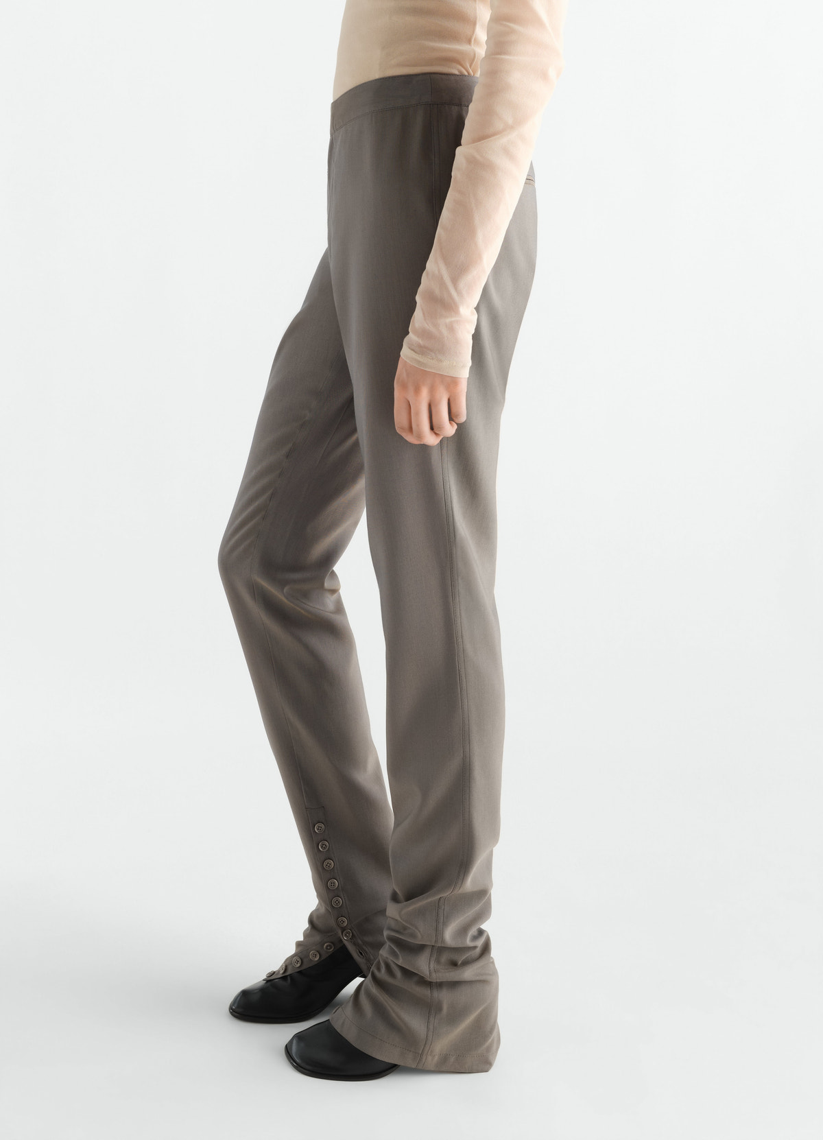 Pantalon tailleur en toile de laine et mohair avec guêtres intégrées, coloris taupe, porté par un mannequin, vue de profil, boutons visibles