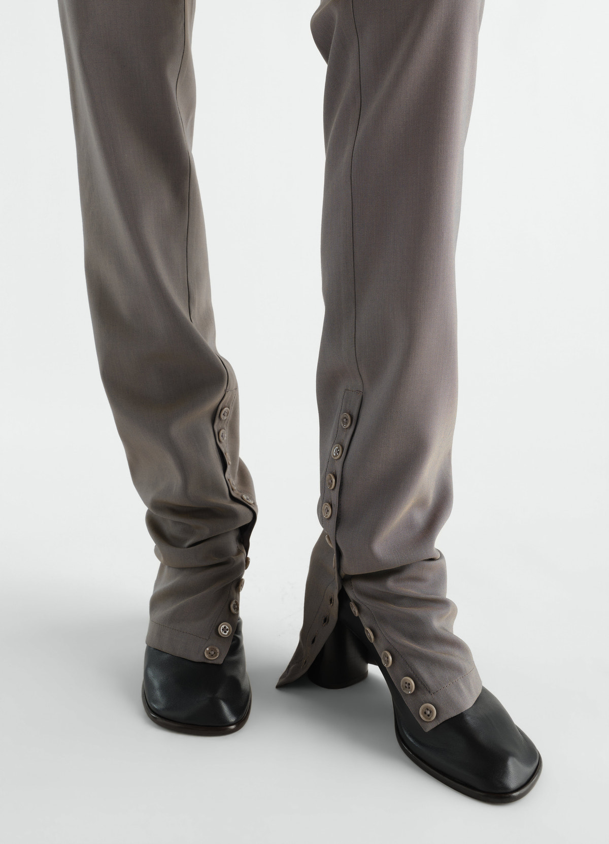 Pantalon tailleur en toile de laine et mohair avec guêtres intégrées, coloris gris, porté par un mannequin, gros plan de face, boutons visibles